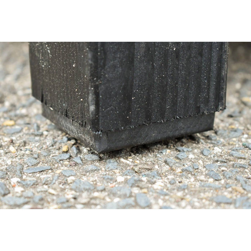 Untere Ecke eines schwarzen, gerippten Kunststoff-Pflanzkübels auf Kiesboden.