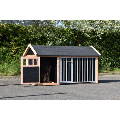 Holz-Hundehütte mit zwei Abschnitten im Garten; links offener Bereich mit liegendem Hund, rechts geschlossener Bereich mit Metallstäben; schwarzes Dach; Hintergrund aus Grünpflanzen.