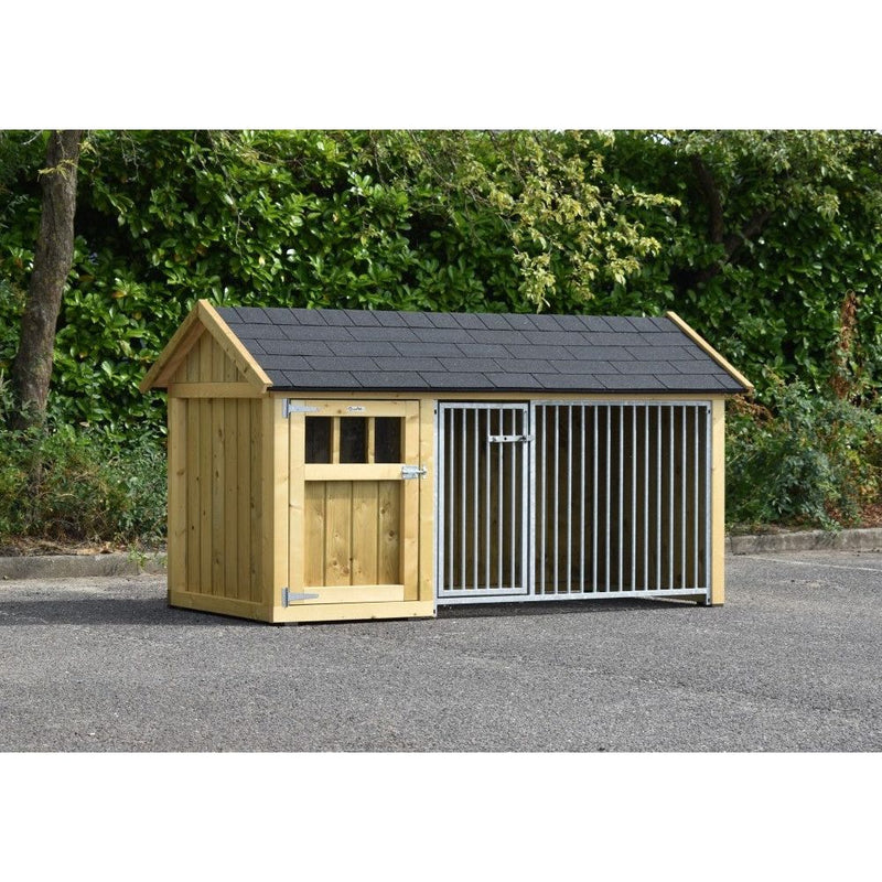 Holz-Hundehütte mit angrenzendem Metall-Zwinger aus senkrechten Stäben, Pultdach mit dunklen Schindeln, auf asphaltierter Fläche vor einer grünen Hecke.
