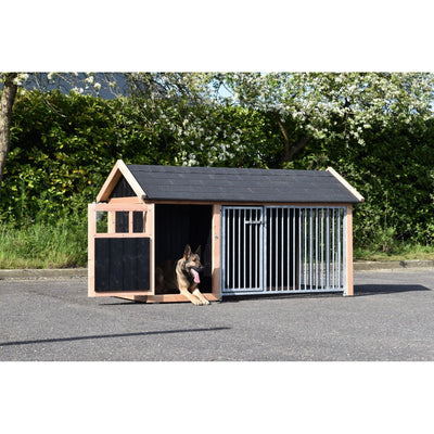 Grosses Holzhundehäuschen mit schwarzem Dach; links offener Eingang, in dem ein Hund liegt; rechts ein Käfigbereich mit vertikalen Metallstäben; Hintergrund aus grüner Hecke und Bäumen.