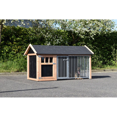 Holz-Hundehütte mit schwarzem Dach und angrenzendem Metall-Laufgitter; Hund im Gehege vor grüner Hecke und blühendem Baum.