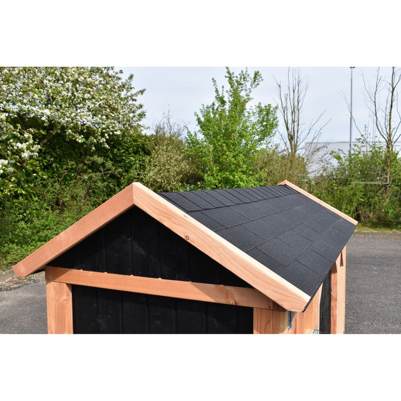 Kleine Gartenhütte aus Holz mit schwarzer Wand und dunklem Schindeldach, umgeben von Bäumen.