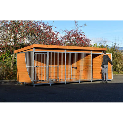 Grosse Hundekäfiganlage aus Holz und Metallrahmen im Freien; eine Person öffnet die Tür rechts; Hintergrund mit Bäumen und blauem Himmel.