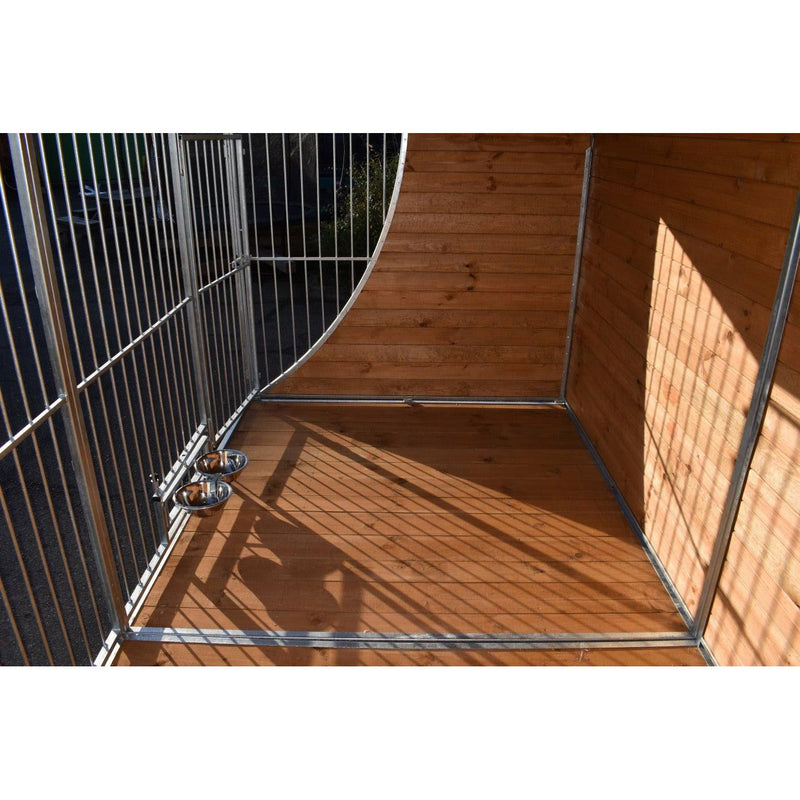 Hundekäfig mit Holzwänden und Metallrahmen, auf einer Holzterrasse; zwei Edelstahl-Näpfe an der linken Wand