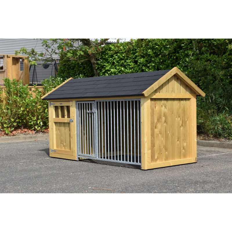Holz-Hundehütte mit schwarzem Dach und Metallgittertür, auf Asphalt, umgeben von Grünpflanzen.