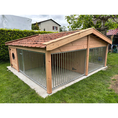 Holz-Hundezwinger mit vertikalen Metallgittern, rotem Ziegeldach und Betonfundament im Garten.