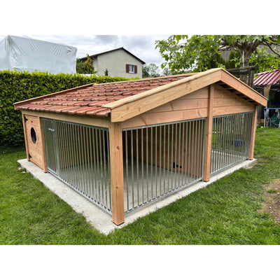 Grosser Outdoor-Hundezwinger aus Holz mit Metallstäben und rotem Ziegeldach, steht auf einer Betonplatte im Garten.