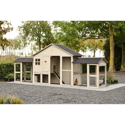 Grosser Holzhühnerstall mit mehreren Gehegeabschnitten und Rampe, Drahtgitter-Auslauf, steht auf Kiesboden in einem Garten mit Bäumen; mehrere Hühner sind im Gehege zu sehen.