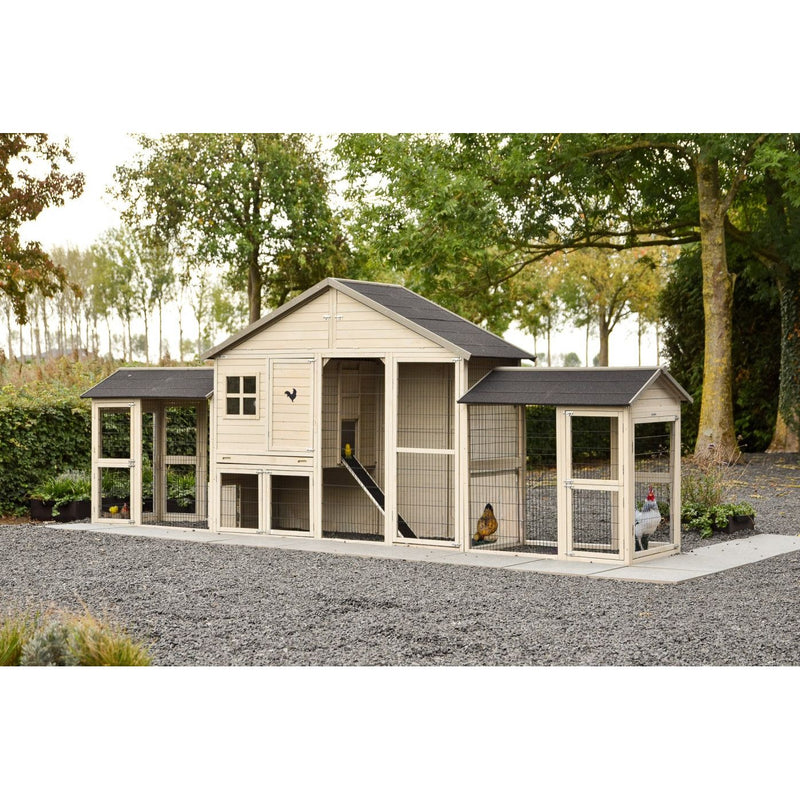 Grosser Holzhühnerstall mit mehreren Gehegeabschnitten und Rampe, Drahtgitter-Auslauf, steht auf Kiesboden in einem Garten mit Bäumen; mehrere Hühner sind im Gehege zu sehen.