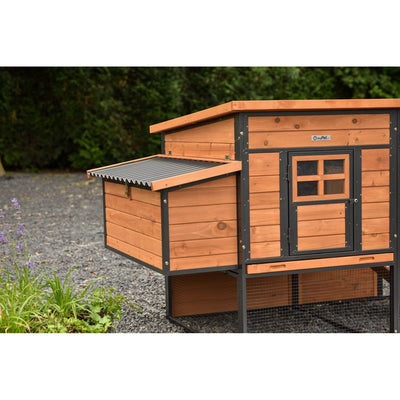 Holz-Hühnerstall mit schwarzem Metallrahmen, kleinem Fenster, seitlichem Anbau mit Schrägdach; darunter Drahtgehege auf Kiesboden im Garten.