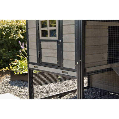 Aussenansicht eines Hühnerstalls aus Holz mit Metallrahmen, kleinem Fenster und Maschendraht-Unterbau, auf Kiesboden im Garten.