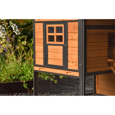 Holz-Hühnerstall mit schwarzem Metallrahmen und Drahtgitter, Tür mit viergeteiltem Fenster, Garten im Hintergrund.