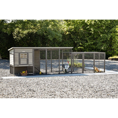 Hühnerstall mit Auslauf aus Drahtgitter, mehrere Gehegeabschnitte auf Kiesboden; Hühner und Hahn im Gehege, grüne Bäume im Hintergrund.