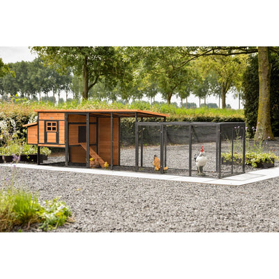 Holz-Hühnerstall mit orangefarbenem Dach und angrenzendem schwarzen Metallgehege; mehrere Hühner und ein Hahn im Gehege in einem Garten mit Bäumen.