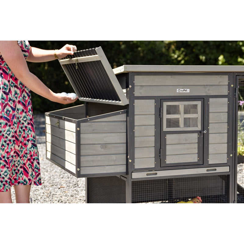 Person sammelt Eier aus einem Holzhühnerstall im Garten; der Stall hat eine seitliche Aufbewahrungskiste und eine kleine Fenstersfront.