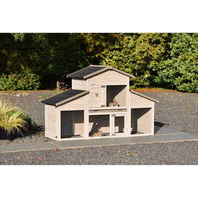 Mehrstöckiger Holz-Kaninchenstall mit Drahtgitter und drei Abteilen, zwei Kaninchen im Innenbereich; Gartenszene mit Kiesweg und grünem Buschwerk im Hintergrund.