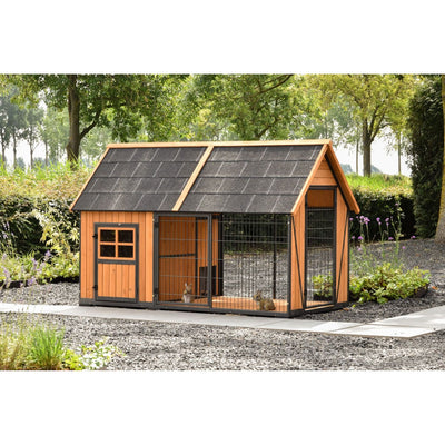 Holz-Hundehütte mit integriertem Drahtgehege, zweigeteiltes dunkles Schindeldach, steht auf Kiesweg im Garten mit Bäumen und Sträuchern.