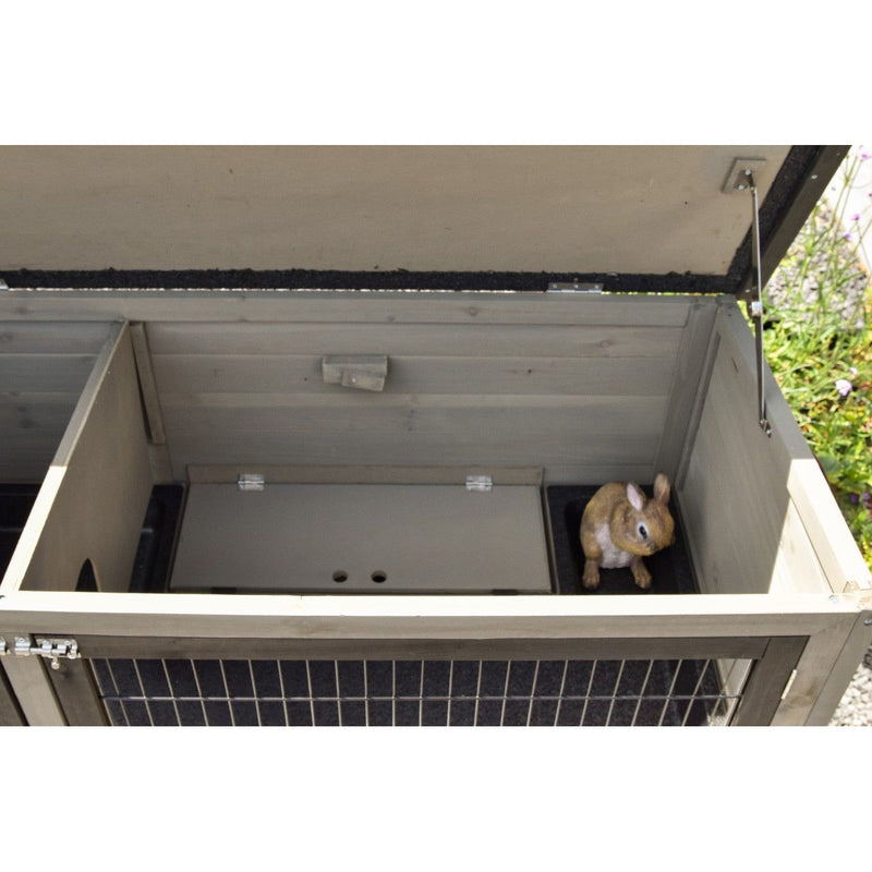 Offenes Holzgehege für Kleintiere mit Gitternetzfront; innen rechts sitzt ein kleines braunes Kaninchen.