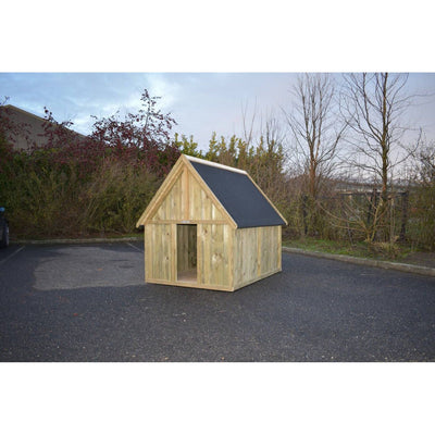 Kleines freistehendes Holzspielhaus mit spitzem dunklem Dach auf Asphalt, umgeben von Büschen und Bäumen.