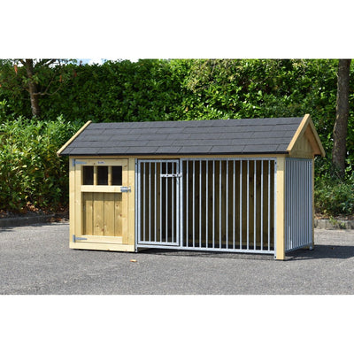 Hundehütte mit Holzrahmen und integriertem Metallkäfig, graues Schindeldach, Tür mit Schloss links, steht auf Asphalt vor grünem Buschwerk.