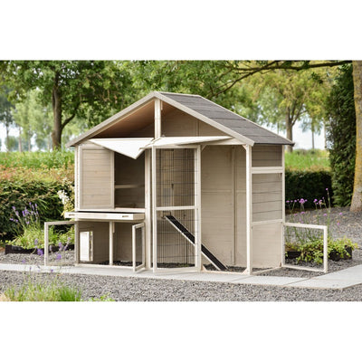 Holz-Hühnerstall mit Drahtgehege und Rampe im Garten auf Kies, umgeben von Bäumen und Blumen.