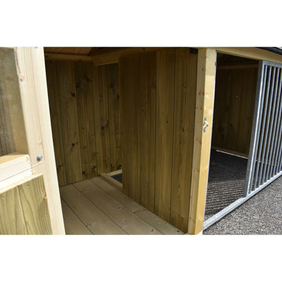 Innenraum eines Holzschuppens mit vertikalen Holzwänden, hellem Holzboden, offener Tür und angrenzendem Metallgitterabschnitt.