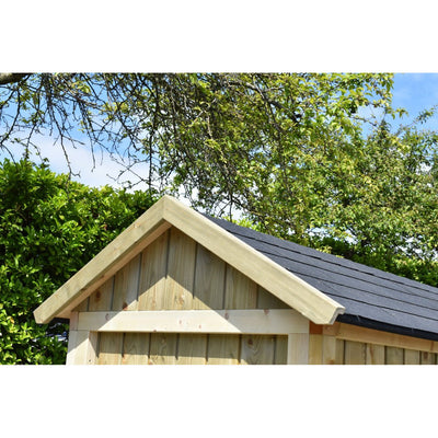 Kleines Gartenhaus aus Holz mit Satteldach und dunkler Dachdeckung, umgeben von grünem Gebüsch und Bäumen vor blauem Himmel.
