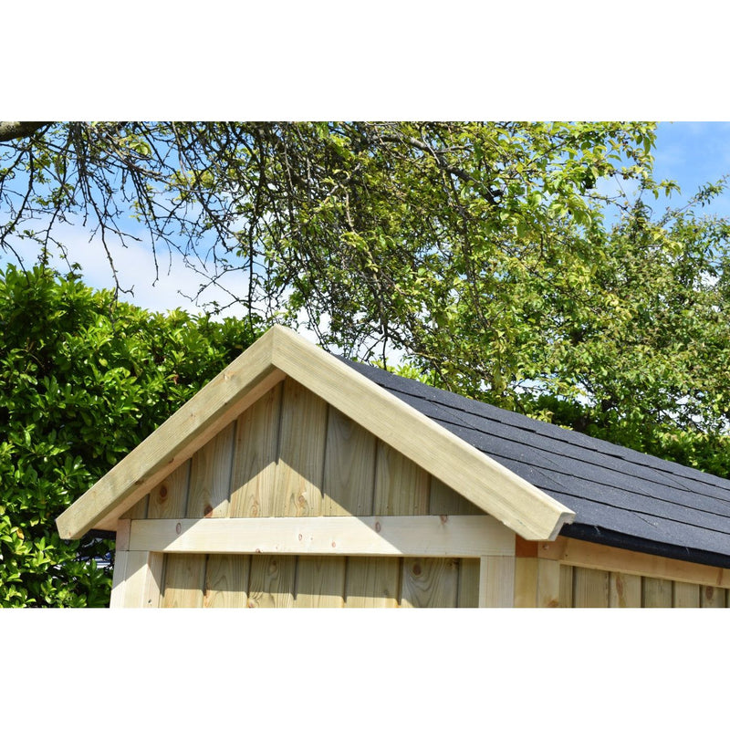 Kleines Gartenhaus aus Holz mit Satteldach und dunkler Dachdeckung, umgeben von grünem Gebüsch und Bäumen vor blauem Himmel.