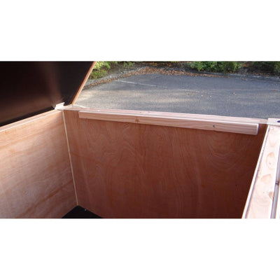 Offene Sperrholz-Holzkiste mit angehobenem Deckel; Innenwand aus Holz, obere Leiste am Rand, Aussenbereich mit Asphalt im Hintergrund.