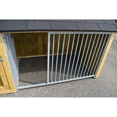 Aussenzwinger aus Holz mit vertikalen Metallstäben und offener Gittertür, auf asphaltiertem Boden unter einem Schindeldach.