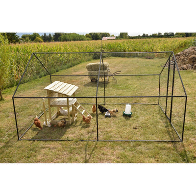 Grosses Hühnergehege aus Metallnetz mit Holzhäuschen und Leiter auf grasbewachsener Wiese; mehrere Hühner erkunden das Gelände, daneben Tränke und Futterautomat, Hintergrund Maisfeld und Heuhaufen.