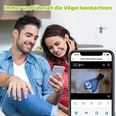 Paar sitzt entspannt auf dem Sofa und schaut auf ein Smartphone; der Bildschirm zeigt die App „Smart Bird Feeder Camera“ mit einem Vogel im Live-Feed.
