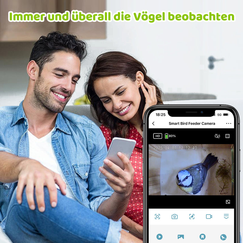 Paar sitzt gemütlich auf der Couch und schaut lächelnd auf ein Smartphone; im oberen Bildbereich steht der Text „Immer und überall die Vögel beobachten“; das Smartphone zeigt die App „Smart Bird Feeder Camera“ mit einer Live-Ansicht eines Vogels.